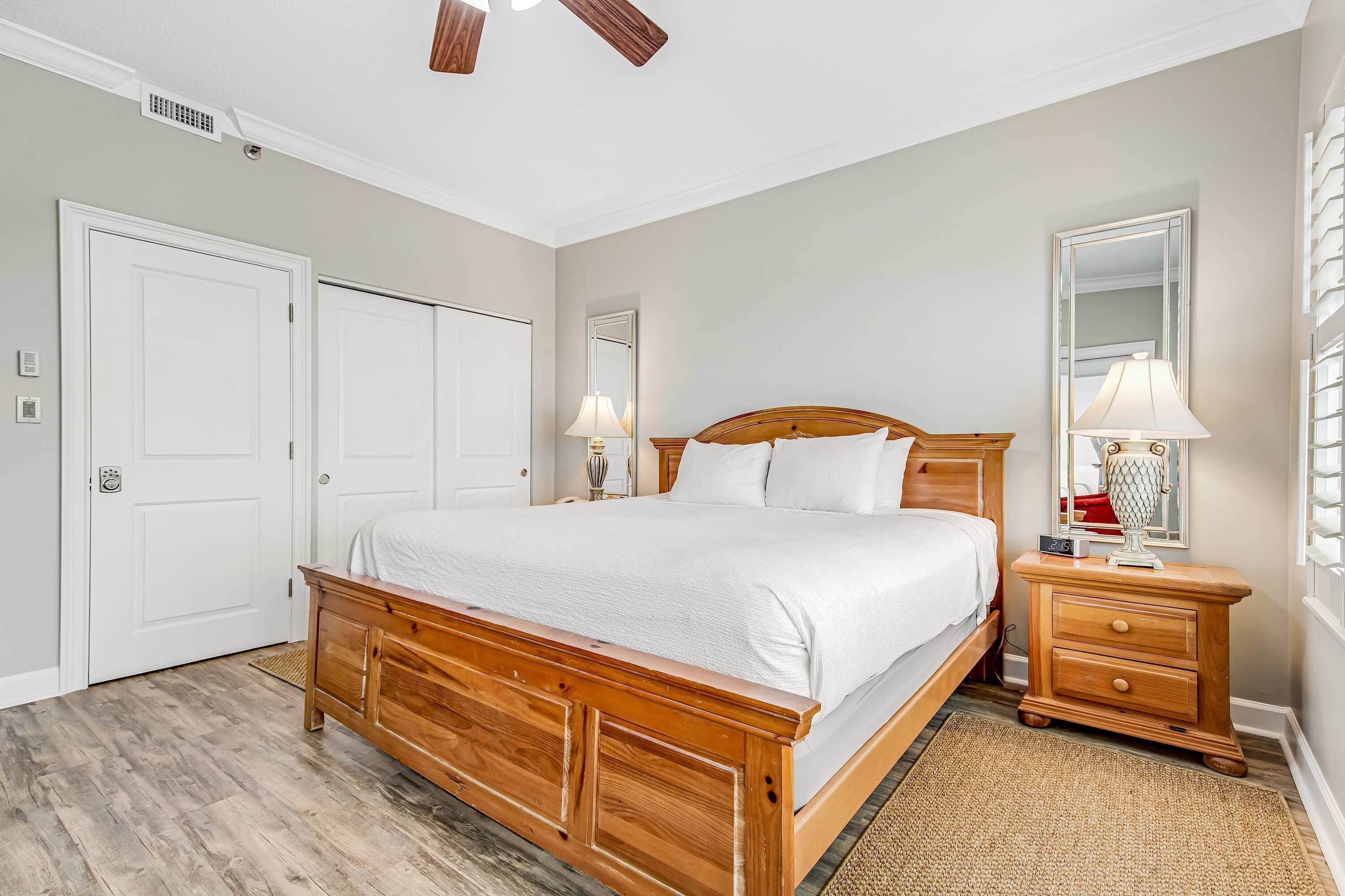 A bedroom with a wooden bed, two bedside tables, a nightstand, a mirror, and a ceiling fan.