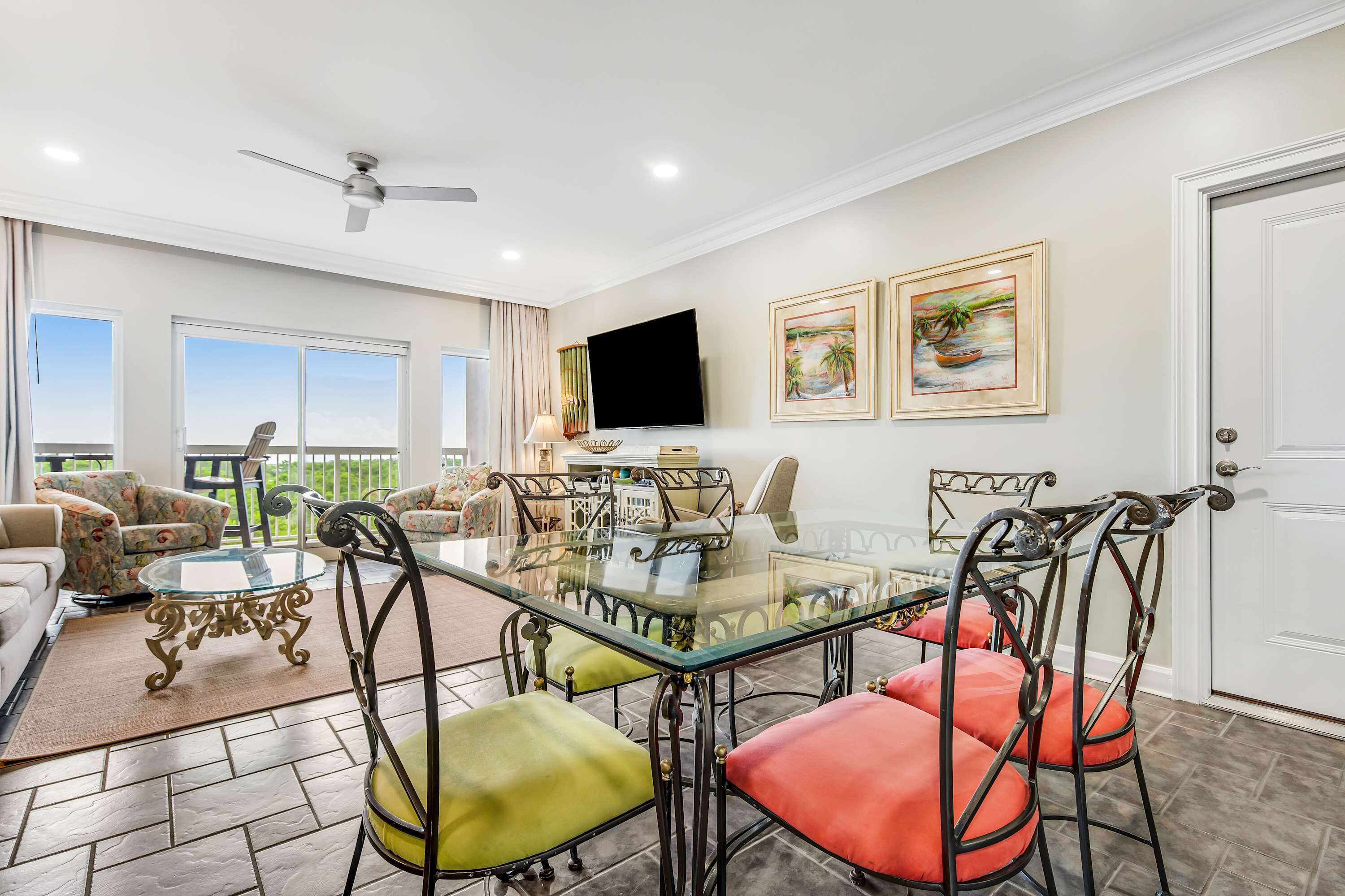 A dining area with a glass-top table, metal chairs, and a television mounted on the wall.