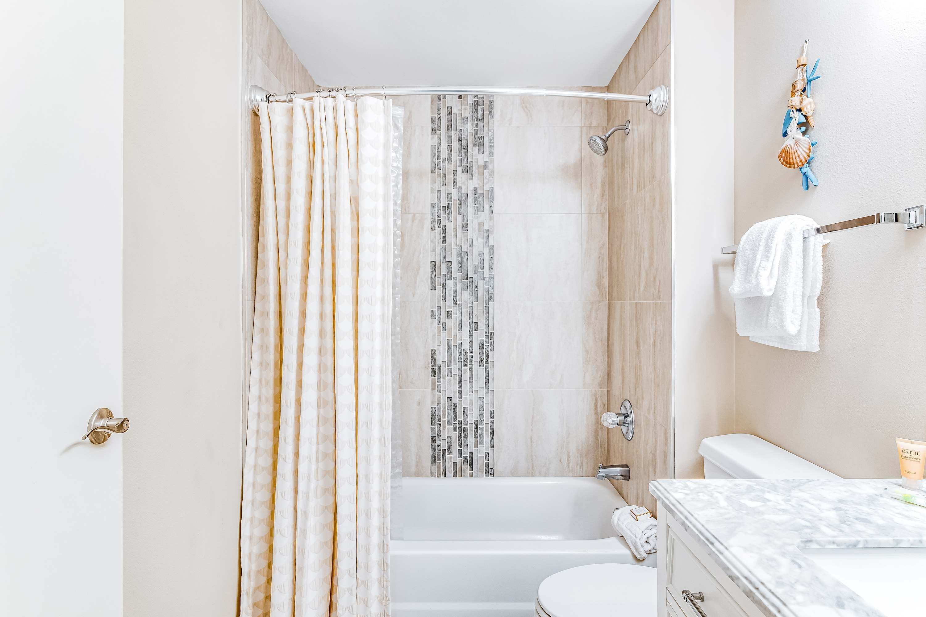 A bathroom with a shower curtain, a bathtub, a toilet, and a sink with a marble countertop.
