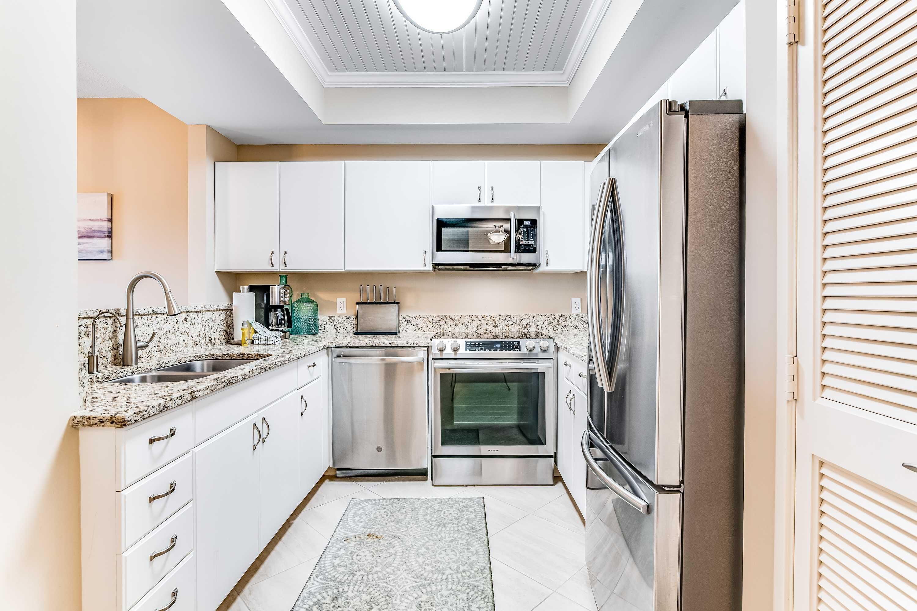 A modern kitchen with white cabinets, stainless steel appliances, and a patterned rug.
