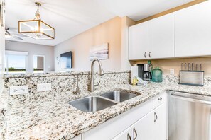 A kitchen with granite countertops, stainless steel appliances, white cabinets, and a pendant light. - Exclusive Gulf-view condo with balcony (Miramar Beach)