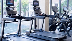 A row of treadmills with digital screens, positioned in front of a window with a view of buildings and trees. - Exclusive Gulf Views: 2BR Beachfront Oasis (Miramar Beach)