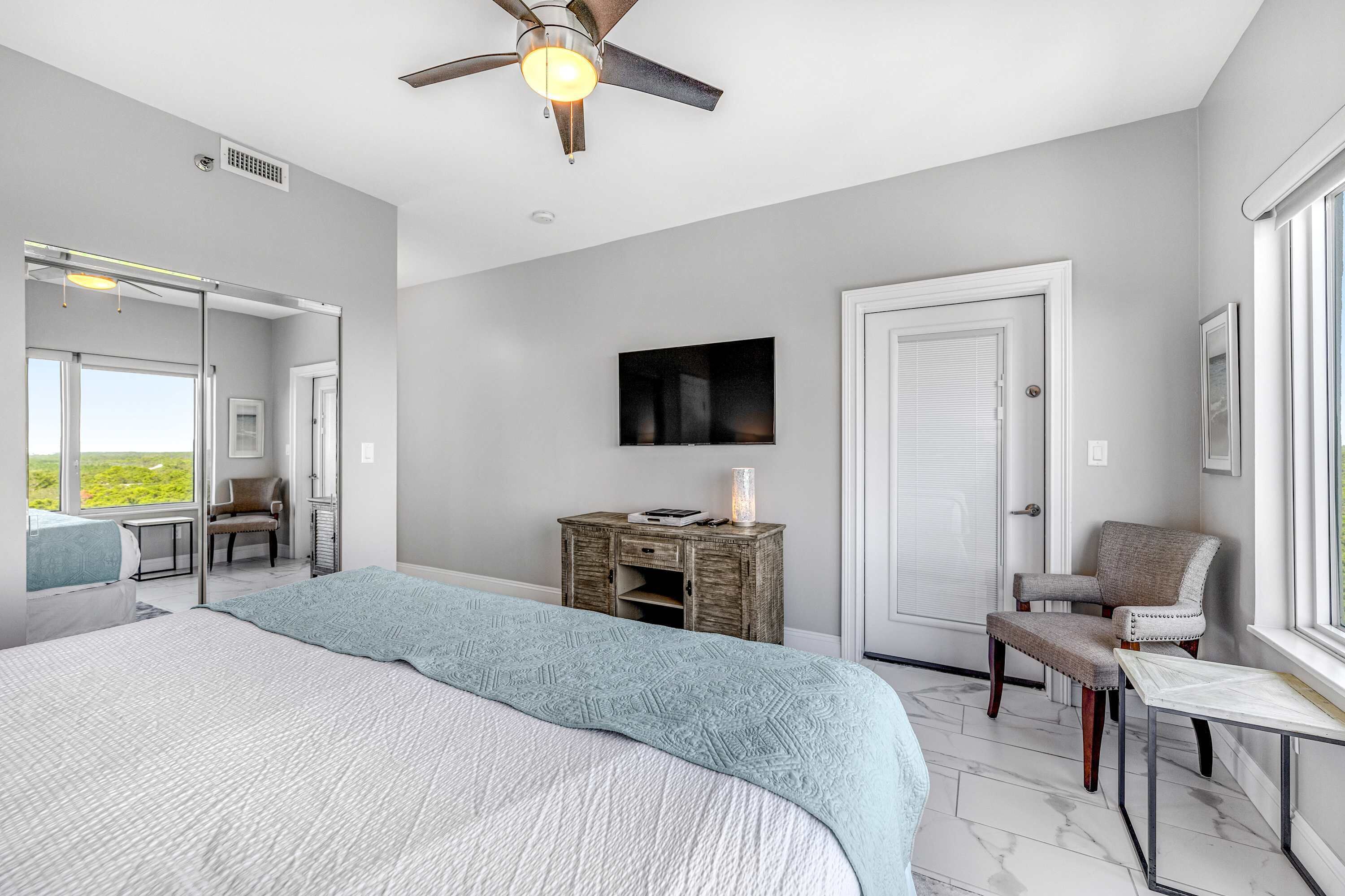 Une chambre à coucher comprenant un lit, un bureau, une chaise, un ventilateur de plafond, une télévision et une fenêtre.