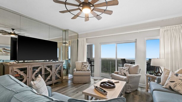 A modern living room with a flat-screen TV, sofas, a coffee table, and a ceiling fan. - 2BR Gulf view condo with resort perks (Miramar Beach)