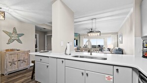 A modern kitchen with a large island, white cabinetry, and a starfish decoration on the wall. - 2BR Gulf view condo with resort perks (Miramar Beach)