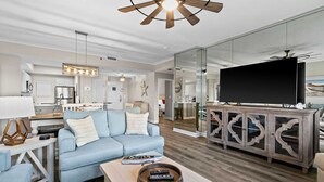 A modern living room with a sofa, coffee table, TV, and a dining area with a kitchen in the background. - 2BR Gulf view condo with resort perks (Miramar Beach)