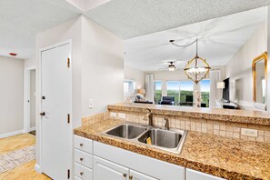 A kitchen with granite countertops, stainless steel sinks, and a ceiling fan. - Steps to Beach | Scenic Views | Resort Amenities (Miramar Beach)