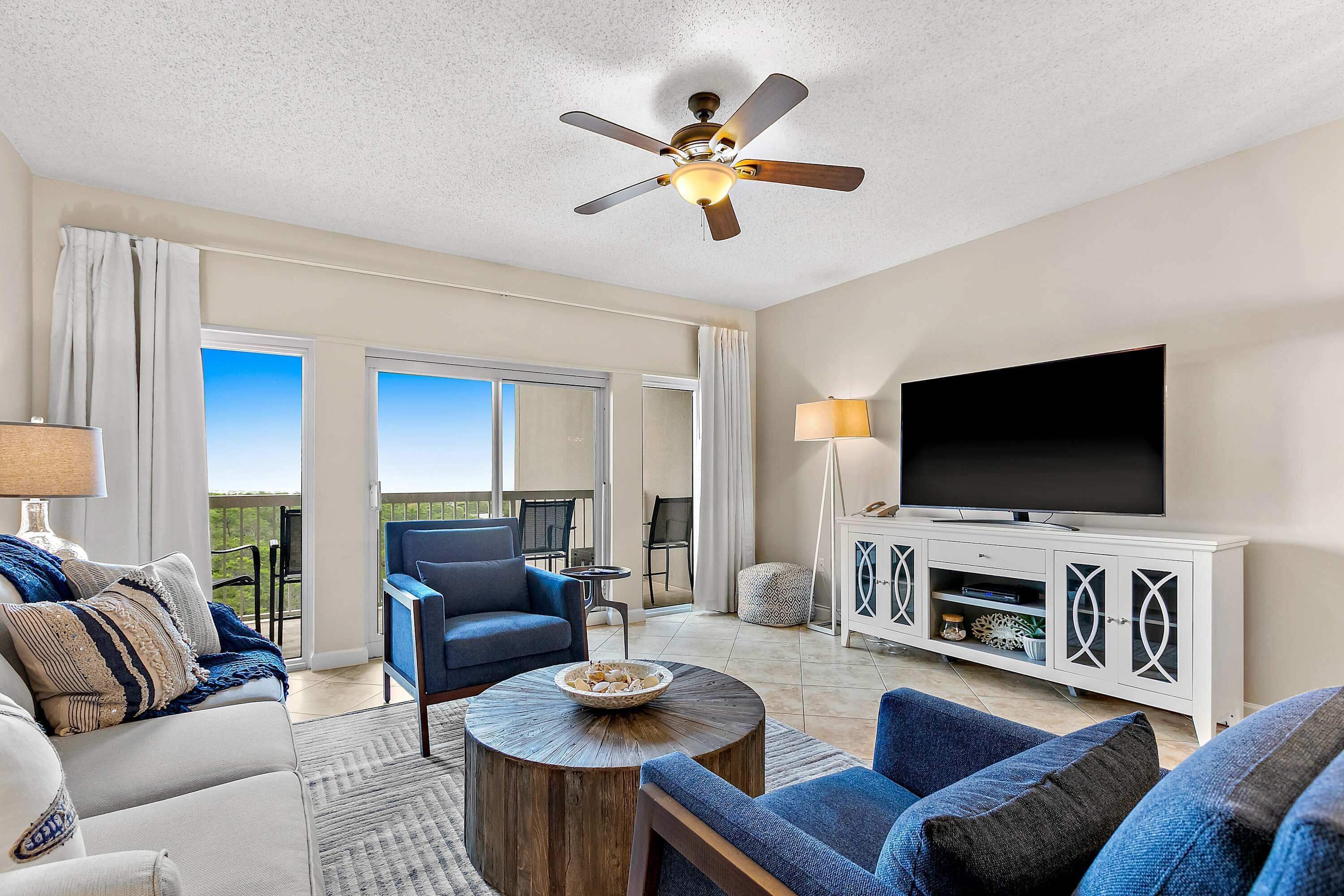 Ein Wohnzimmer mit Deckenventilator, Fernseher, Sofa, Couchtisch und einem Balkon mit Blick.