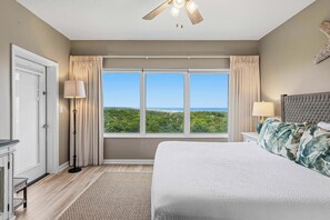 A bedroom with a large bed, a ceiling fan, a view of the outdoors, and a window with curtains. - Private balcony, resort pool & beach access (Miramar Beach)