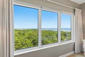 A room with a large window offering a view of a forest and a beach. - Private balcony, resort pool & beach access (Miramar Beach)