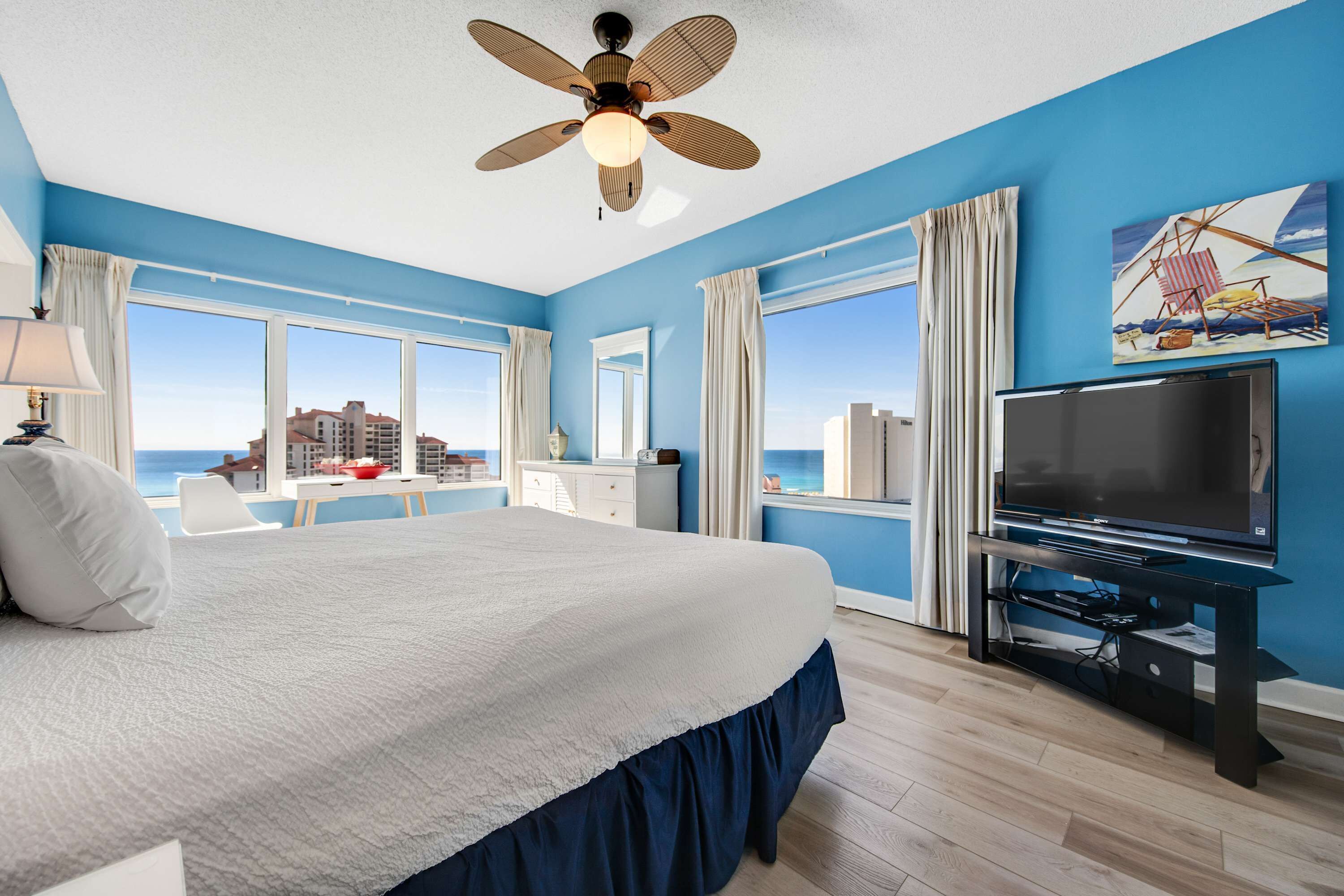A hotel room with a bed, a television, a desk, and a view of the ocean.