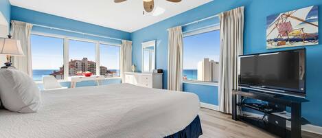A hotel room with a bed, a television, a desk, and a view of the ocean.