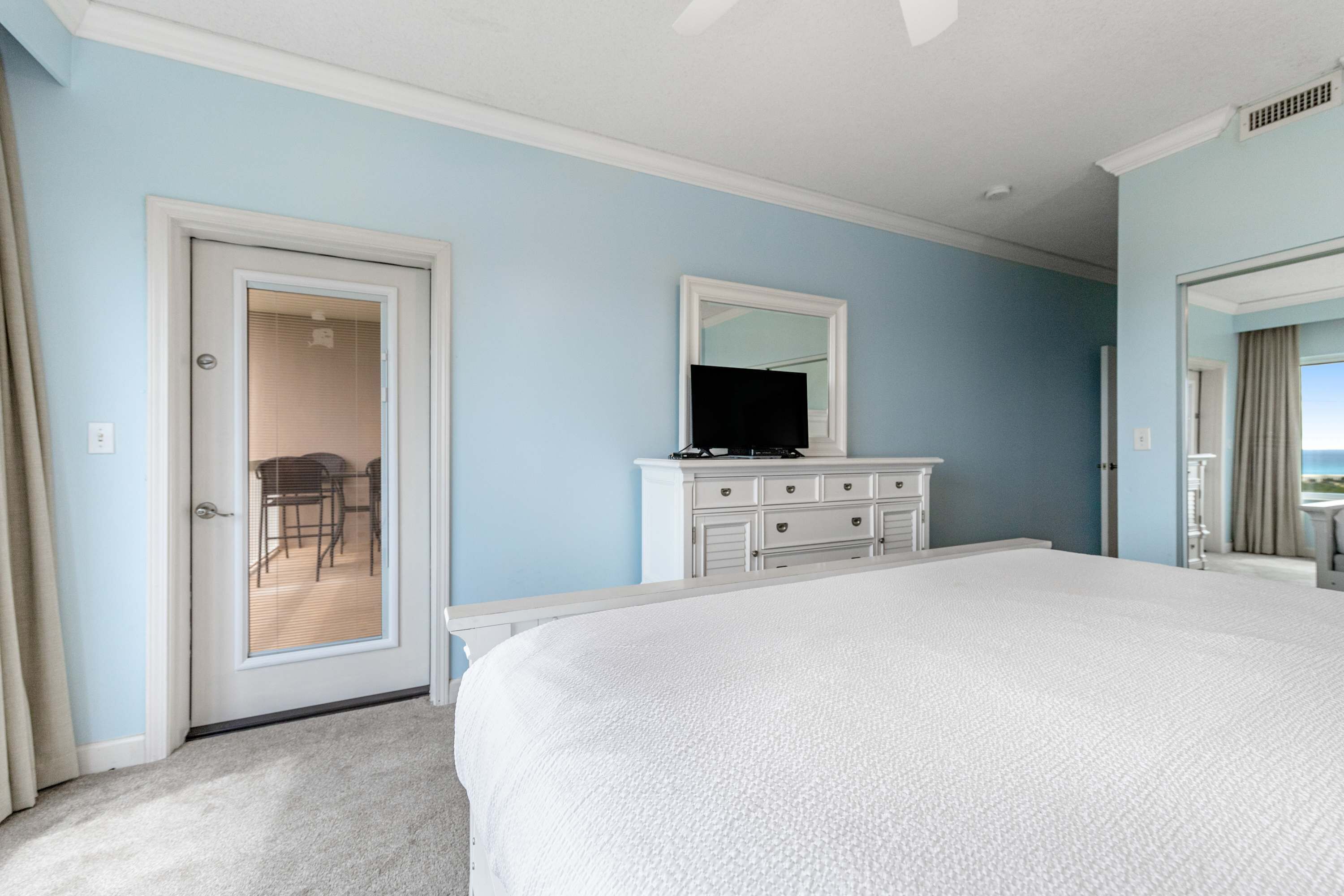 A bedroom with a bed, a dresser, a mirror, and a door leading to a balcony.