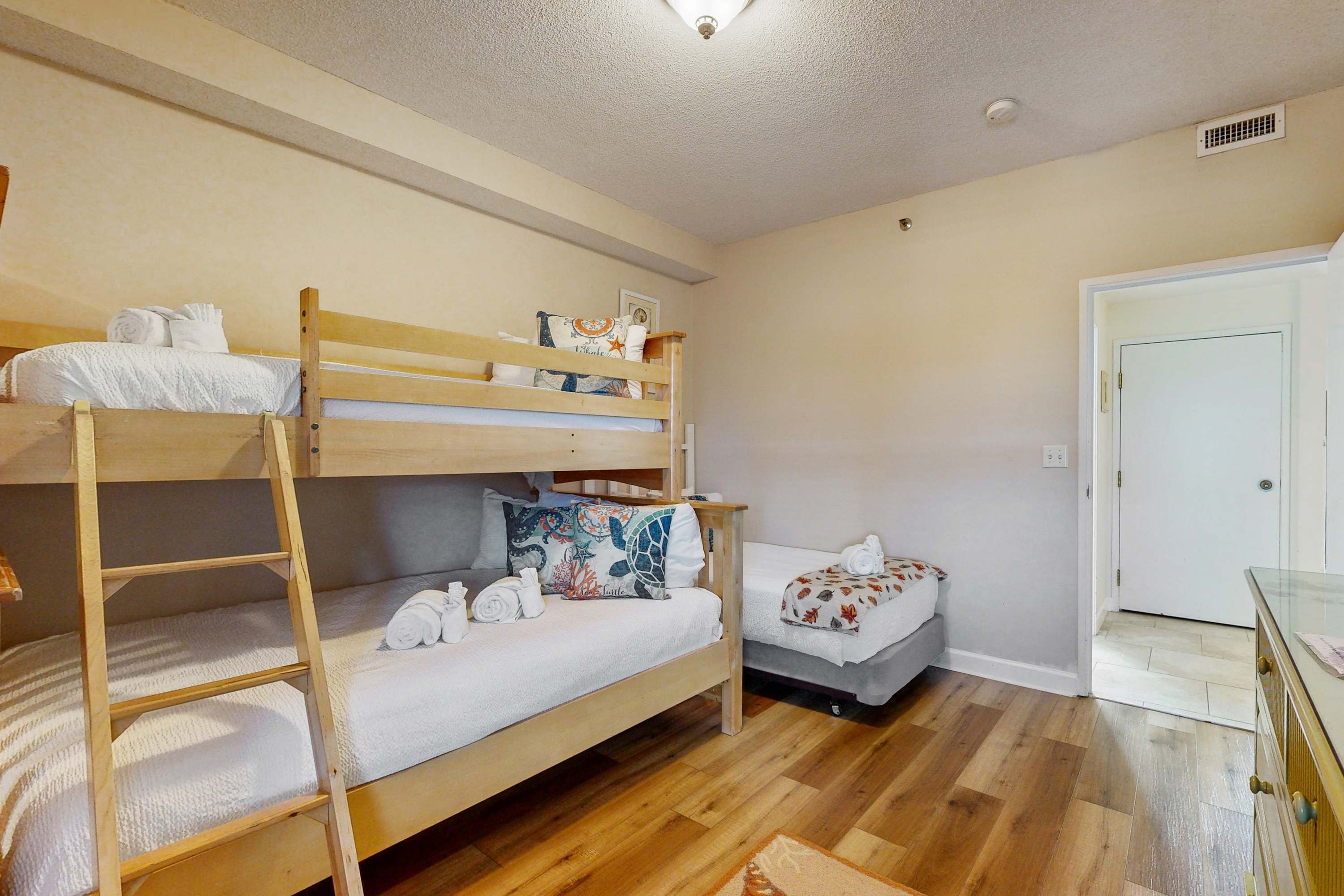 Een slaapkamer met een stapelbed, een houten ladder, een bureau en een deur.