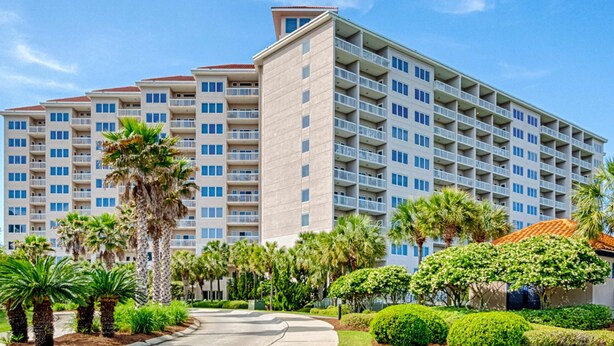 Un hotel de varios pisos con balcones, rodeado de palmeras y jardines bien cuidados.