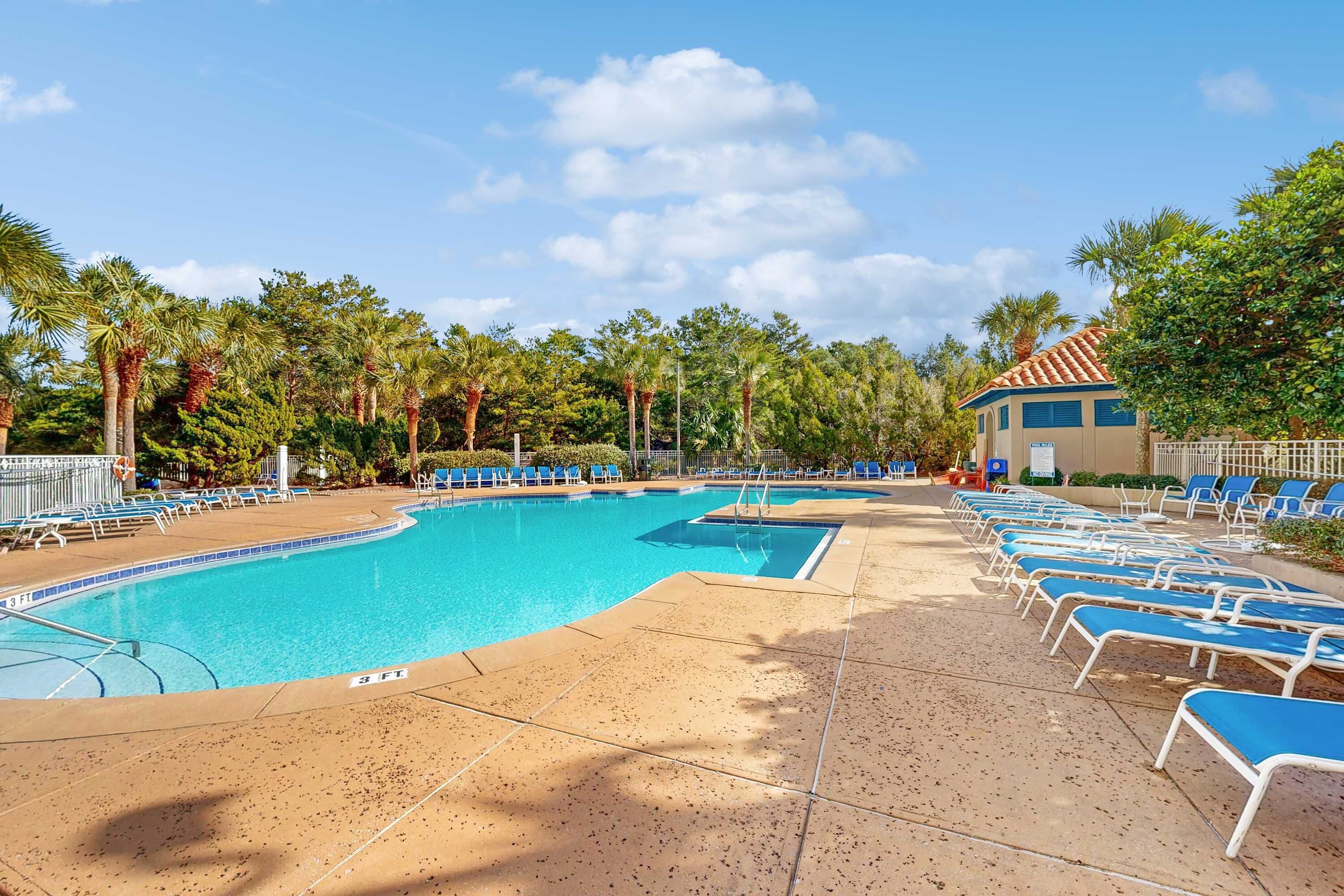 Una piscina con sillas de descanso, palmeras y un edificio con techo de tejas.