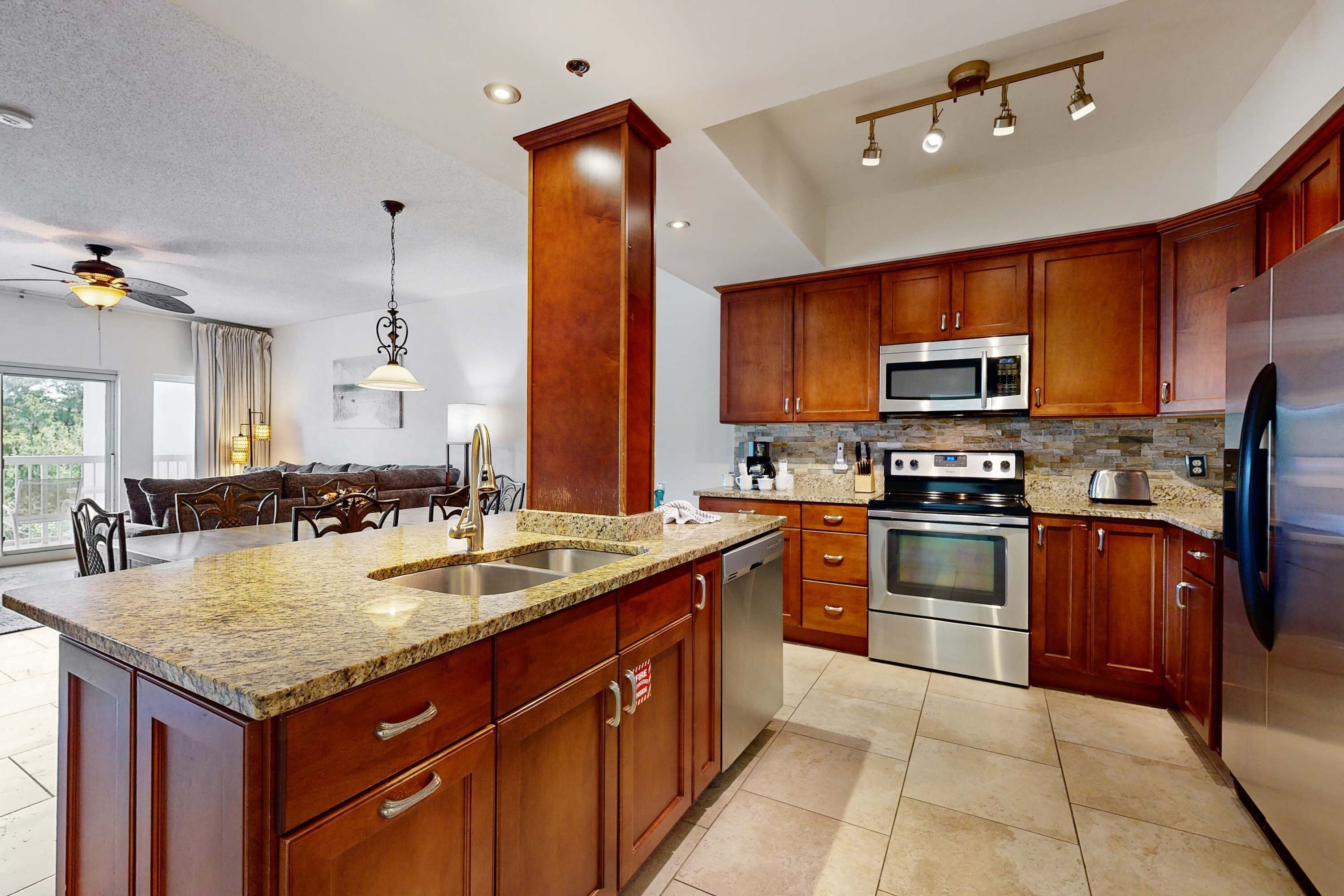 A kitchen with granite countertops, stainless steel appliances, wooden cabinets, and a dining area with a chandelier.