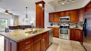 Una cocina con encimeras de granito, electrodomésticos de acero inoxidable, armarios de madera y un comedor con candelabro.