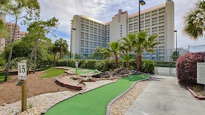 A miniature golf course with a green putting surface, surrounded by a gravel path and landscaped areas. - Beachside studio with pool & hot tub access (Miramar Beach)
