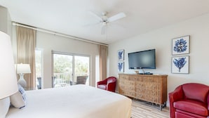 A hotel room with a large bed, a television, a wicker dresser, and a balcony with curtains. - Beachside studio with pool & hot tub access (Miramar Beach)