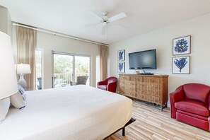 A hotel room with a large bed, a television, a wicker dresser, and a balcony with curtains. - Beachside studio with pool & hot tub access (Miramar Beach)