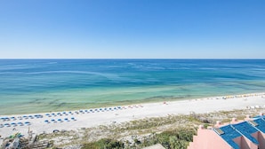 A beach with clear blue water, white sand, and umbrellas. There is a building with a pink roof in the foreground. - Beachside studio with pool & hot tub access (Miramar Beach)
