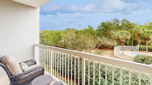 A balcony with wicker furniture, a pool, and a view of greenery. - Beachside studio with pool & hot tub access (Miramar Beach)