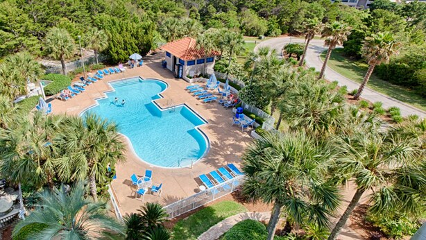 Vista aérea de un resort con una piscina grande, sillas de descanso y palmeras.