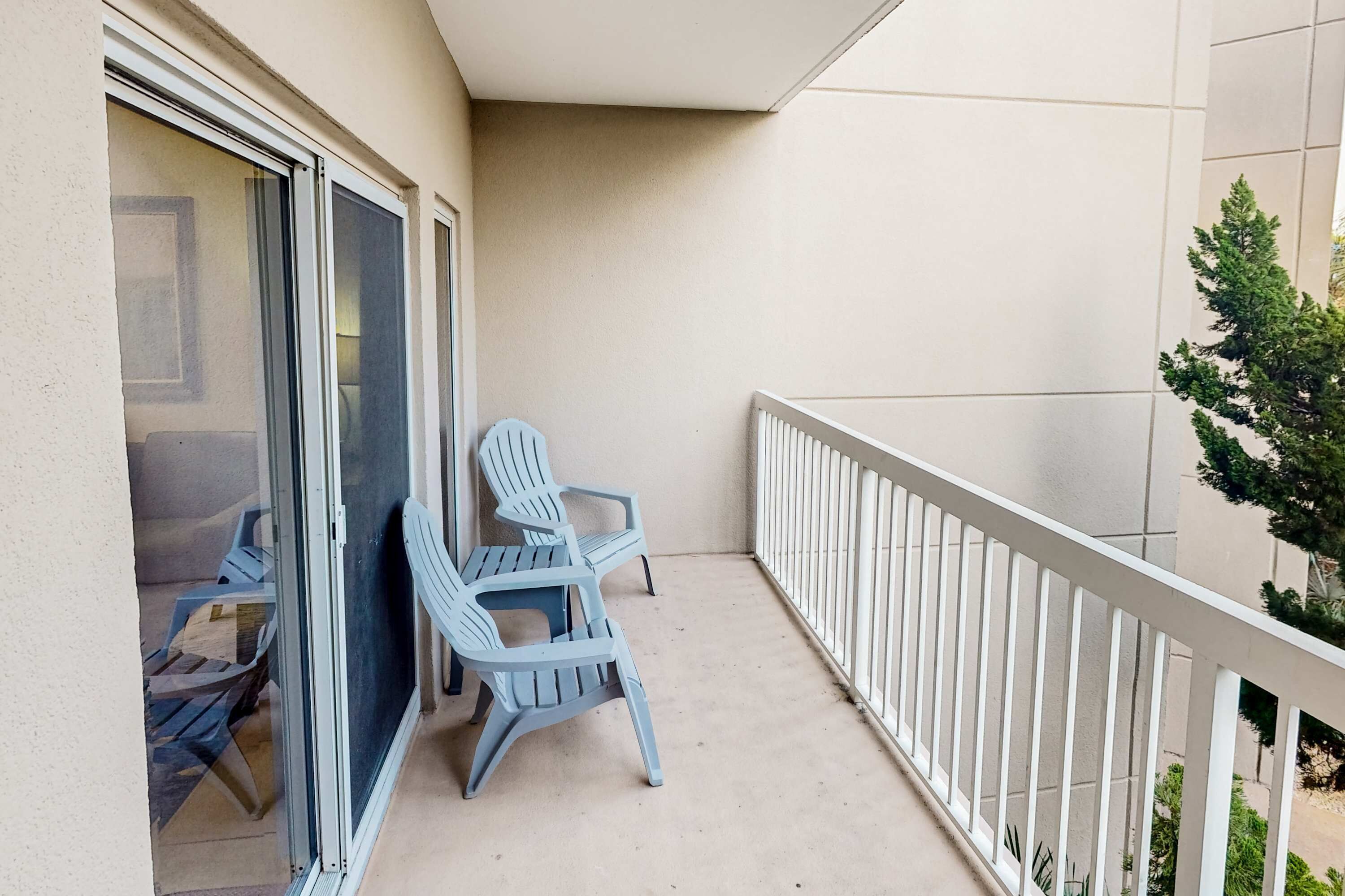 A balcony with a white railing, two blue chairs, and a small potted plant.