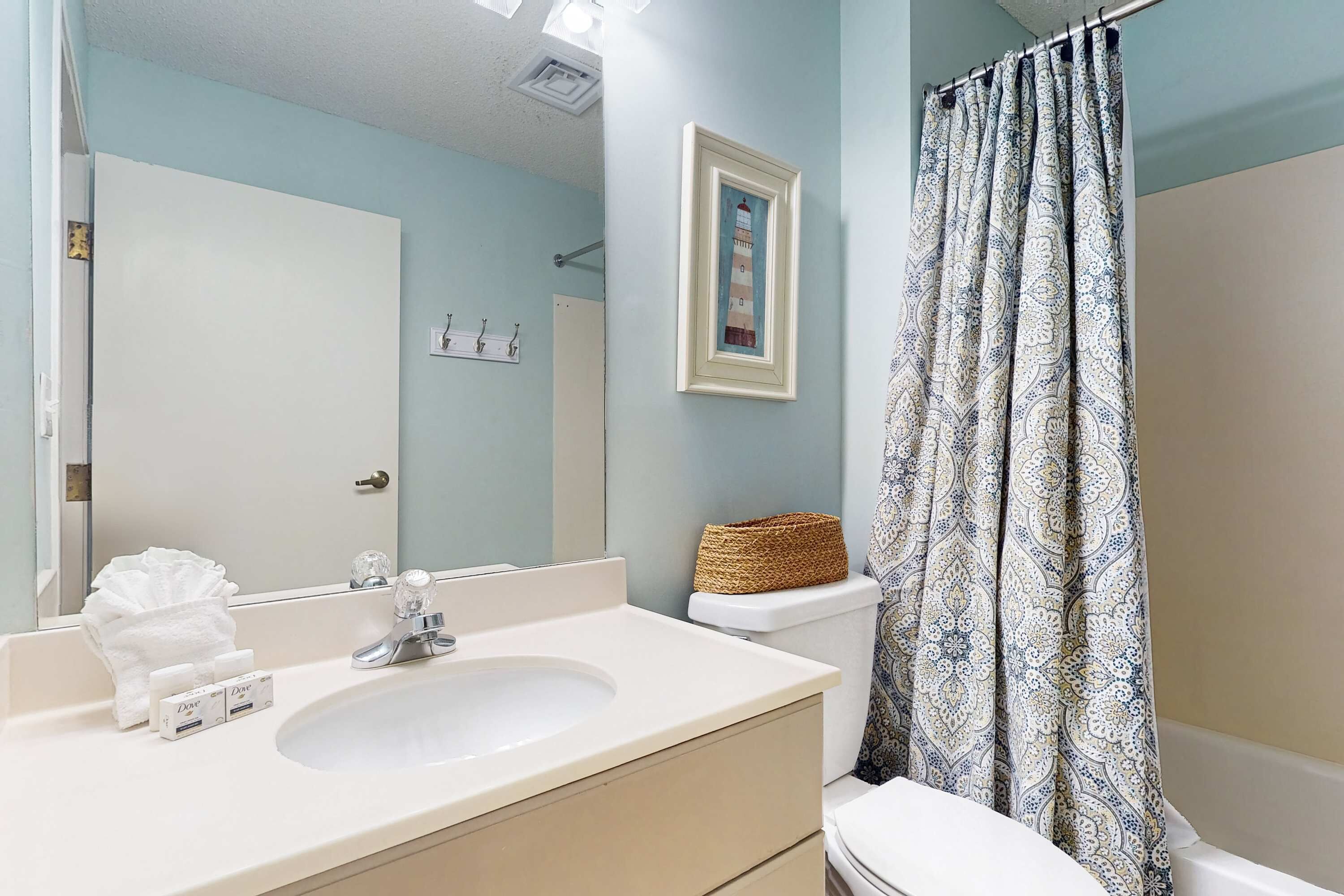 A bathroom with a sink, mirror, toilet, and patterned shower curtain.