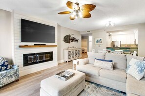 Ein Wohnzimmer mit Kamin, Flachbildfernseher, Deckenventilator und einer Küche im Hintergrund.
