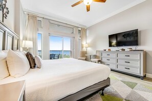 A hotel room with a large bed, a television, a dresser, and a balcony with curtains. - Exclusive Gulf view studio, beach access (Miramar Beach)