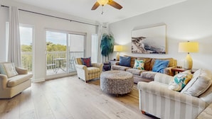 A spacious living room with a ceiling fan, large windows, a balcony, and a variety of seating options. - 2BR condo with pool, hot tub & beach access (Miramar Beach)