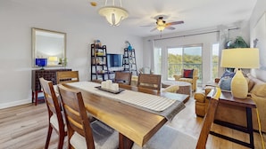 A dining area with a wooden table, chairs, a ceiling fan, and a large window. - 2BR condo with pool, hot tub & beach access (Miramar Beach)