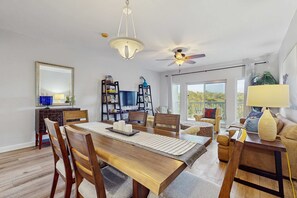 A dining area with a wooden table, chairs, a ceiling fan, and a large window. - 2BR condo with pool, hot tub & beach access (Miramar Beach)