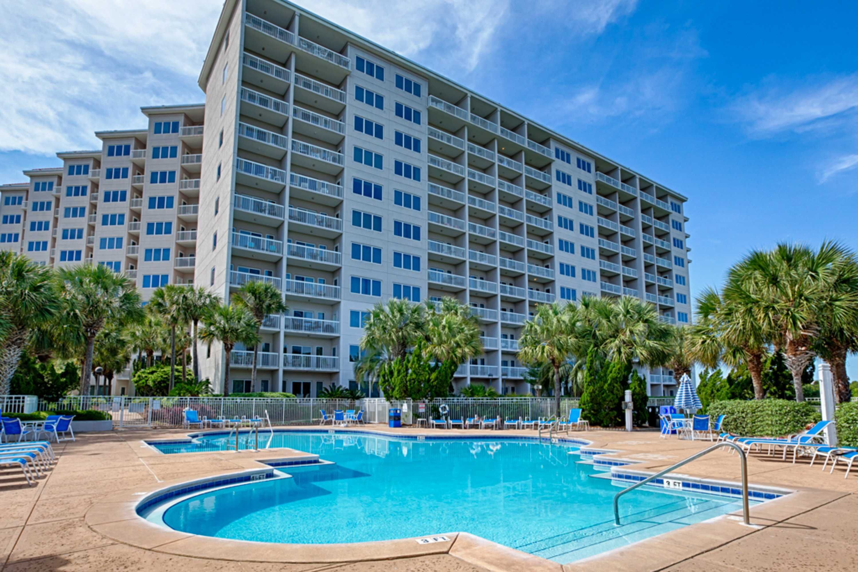 A hotel with a swimming pool, palm trees, and a large building with multiple balconies.
