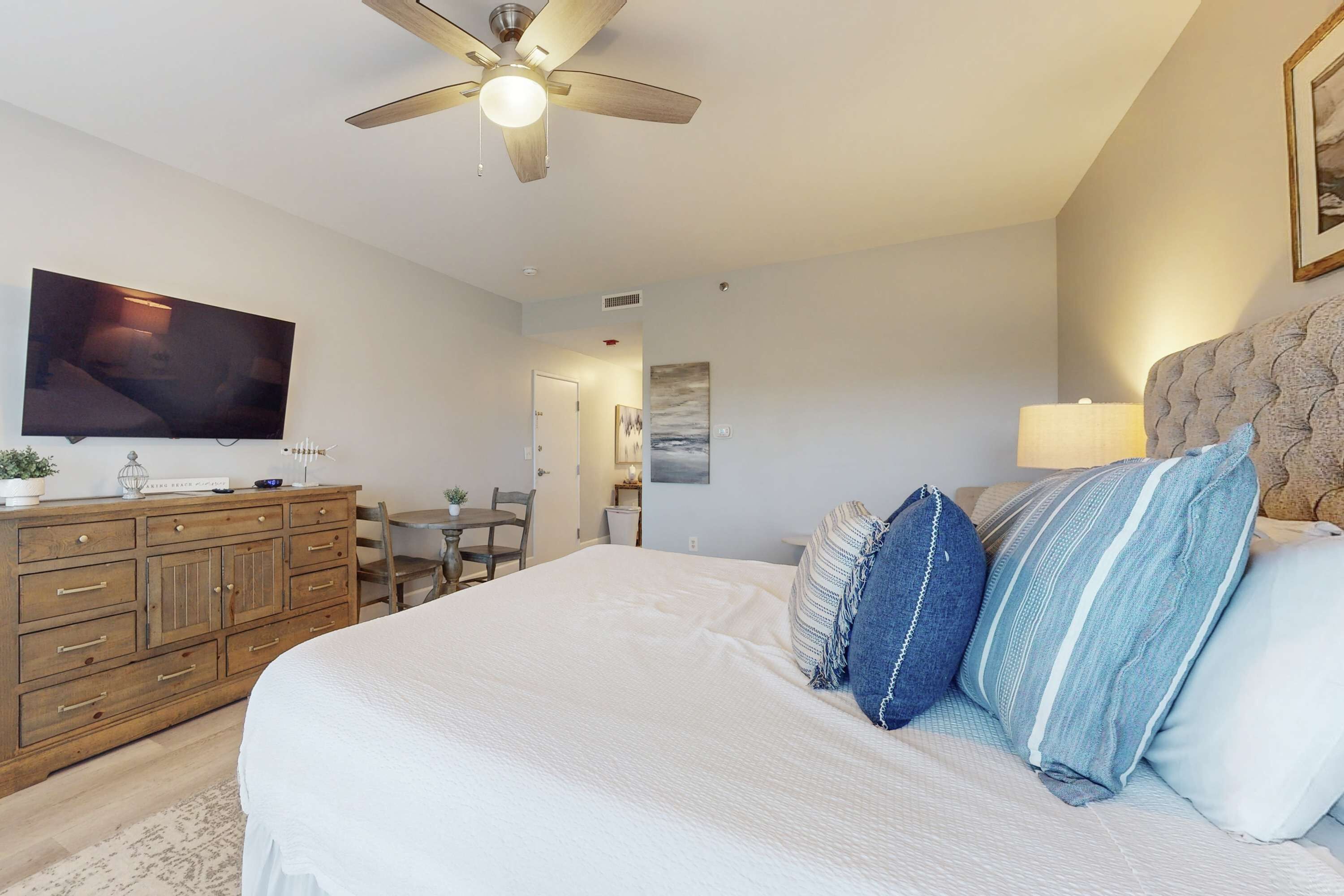 A bedroom with a bed, a ceiling fan, a TV, a dresser, and a dining area.