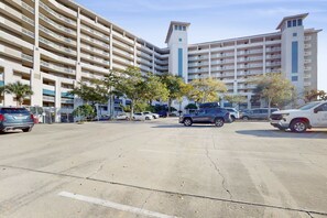 A multi-story parking garage with several cars parked, surrounded by a large building with balconies. - 2BR condo with sunrise views, beach access (Miramar Beach)