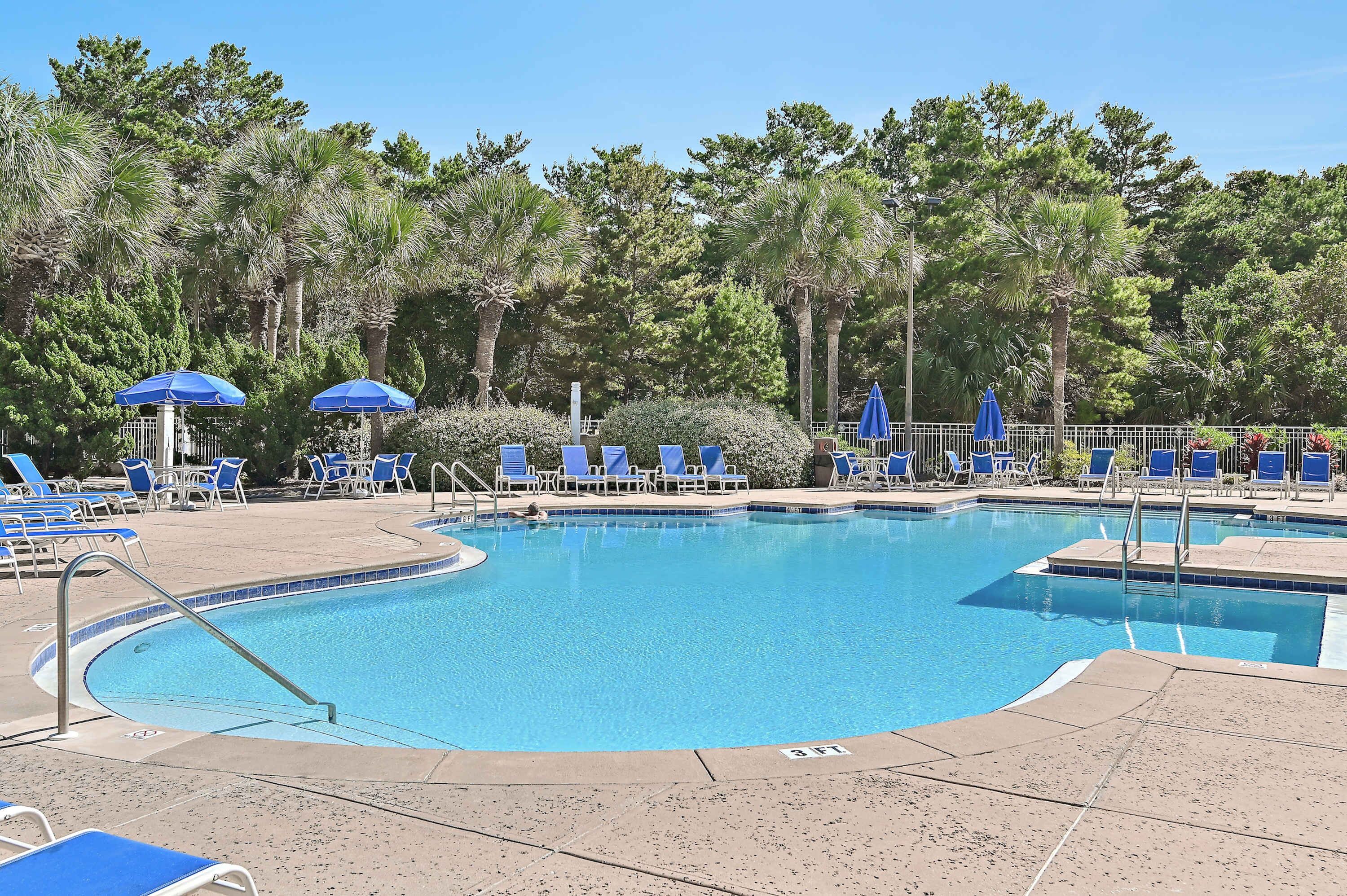 Una piscina con sillas y sombrillas azules, rodeada de árboles.