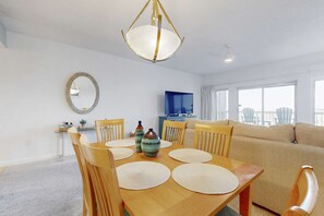 A dining area with a wooden table, chairs, and a hanging light fixture. - 2BR condo with sunrise views, beach access (Miramar Beach)
