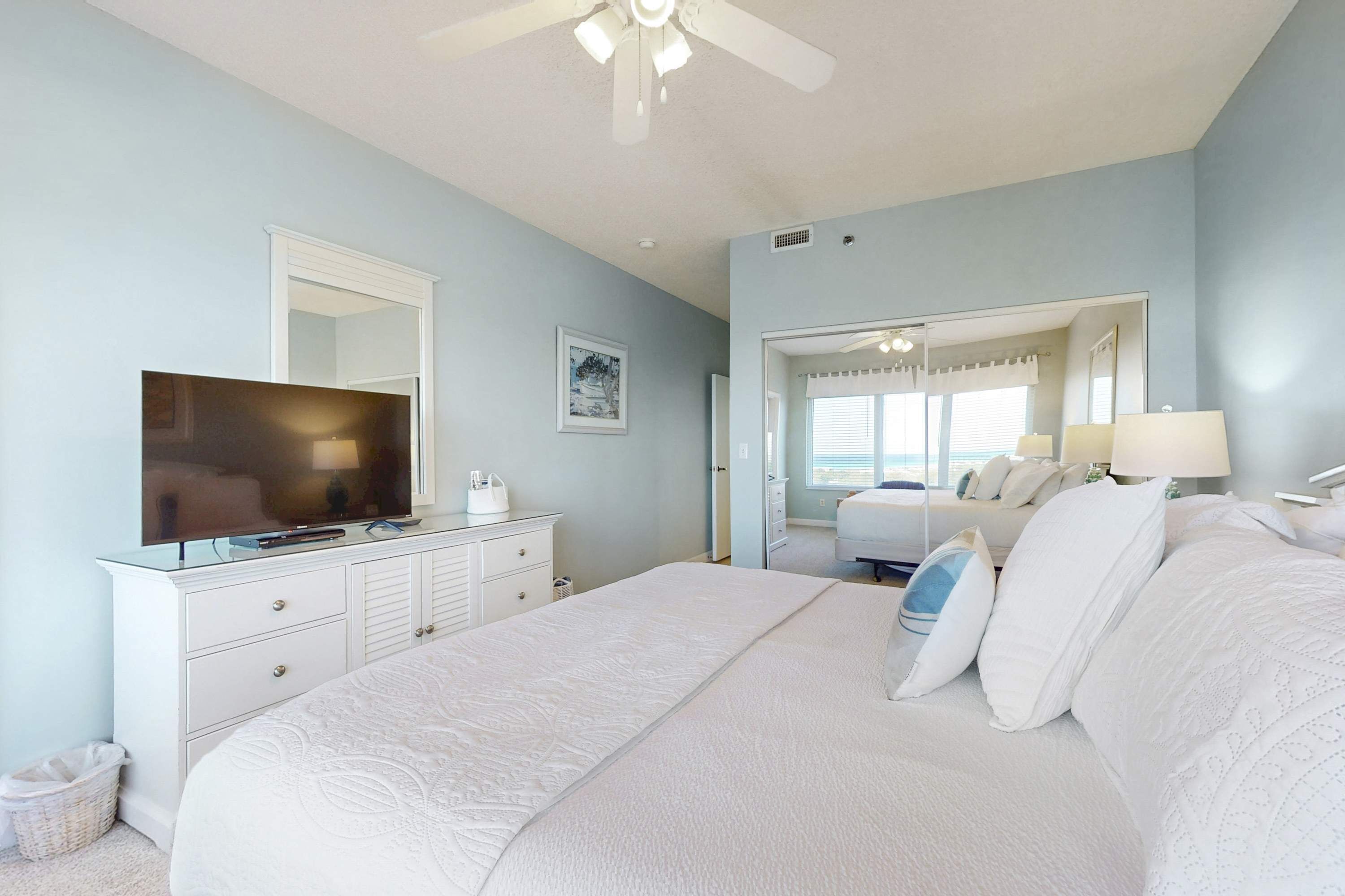 A bedroom with a bed, dresser, television, and a large mirror.