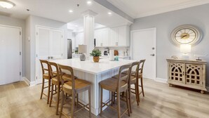 Een moderne keuken met witte kasten, een centraal eiland met barstoelen, en een decoratieve kast met een klok.