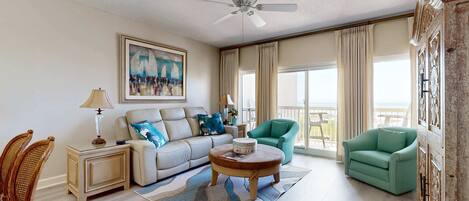 A spacious living room with a sofa, armchair, coffee table, and a ceiling fan.