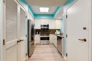 A narrow kitchen with white cabinets, stainless steel appliances, and a teal accent wall. - 2BR condo with Gulf views, pools, tennis (Miramar Beach)