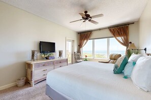 A bedroom with a large bed, a ceiling fan, a television on a dresser, and a view of the ocean. - 2BR condo with Gulf views, pools, tennis (Miramar Beach)