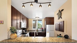 A kitchen with granite countertops, stainless steel appliances, wooden cabinets, and a decorative turtle wall art piece.