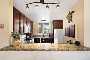 A kitchen with granite countertops, stainless steel appliances, wooden cabinets, and a decorative turtle wall art piece. - NEW LISTING 
Beautiful Kailua Kona 2-bed 2-bath condo w/AC in at KKSRC by beach (Kailua-Kona)