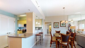 A modern kitchen with a central island, bar stools, and a dining area with wicker chairs. - Exclusive 3BR condo with Gulf views (Miramar Beach)