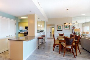 A modern kitchen with a central island, bar stools, and a dining area with wicker chairs. - Exclusive 3BR condo with Gulf views (Miramar Beach)