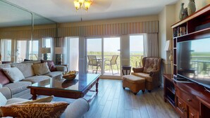 A spacious living room with a large flat-screen TV, comfortable seating, a glass coffee table, and a balcony with a view. - Exclusive 3BR condo with Gulf views (Miramar Beach)